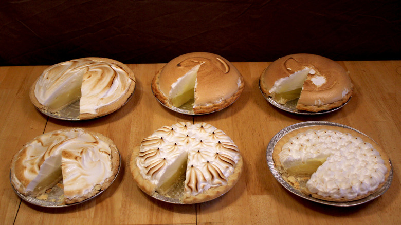 Six store-bought lemon meringue pies on a table each missing a slice