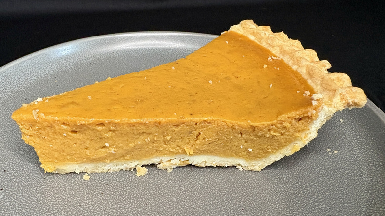 slice of pumpkin pie on gray plate, black background