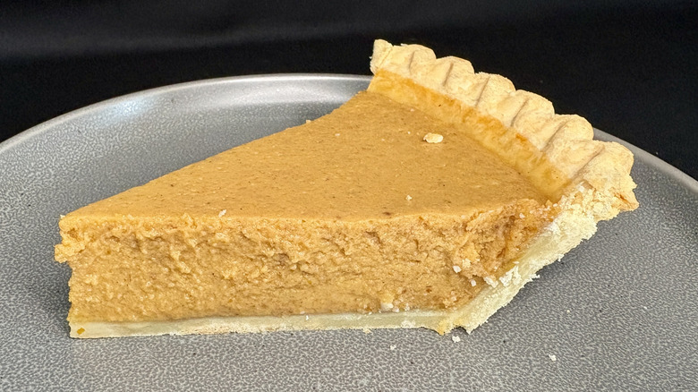 slice of pumpkin pie on gray plate, black background