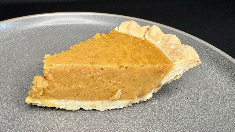 slice of pumpkin pie on gray plate, black background