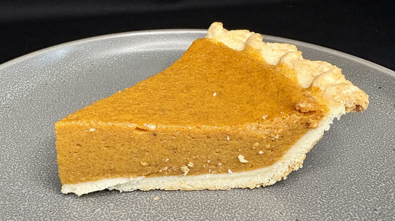 slice of pumpkin pie on gray plate, black background