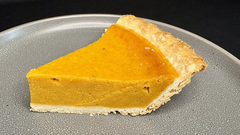 slice of pumpkin pie on gray plate, black background