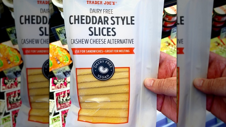 A hand holding a package of Trader Joe's Cheddar-Style Cheese Slices.