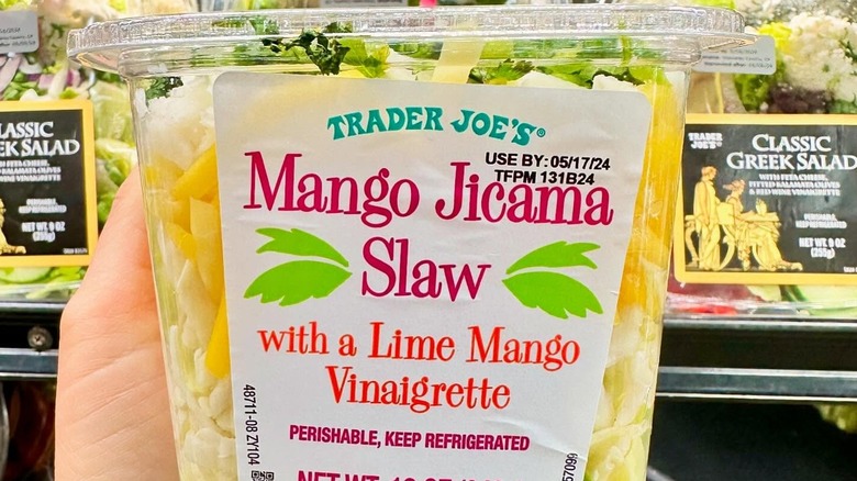 A hand holding a container of Trader Joe's Mango Jicama Slaw.