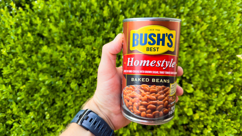 Hand holding a can of Bush's baked beans outdoors
