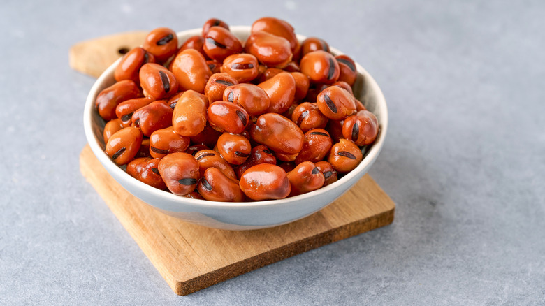 A white bowl on a wooden cutting board filled with cooked fava beans