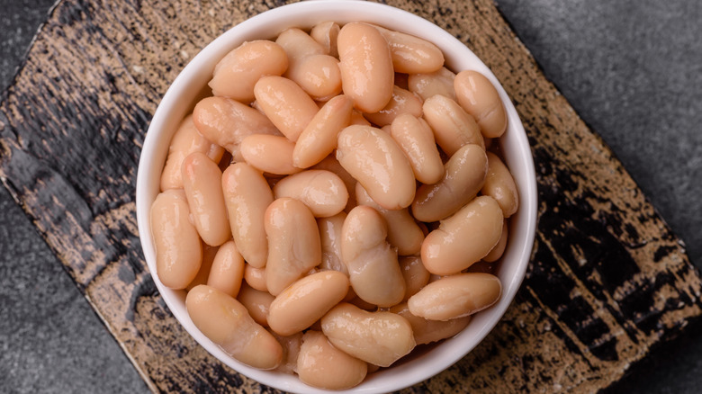 A white bowl on a wooden cutting board filled with cooked white cannellini beans