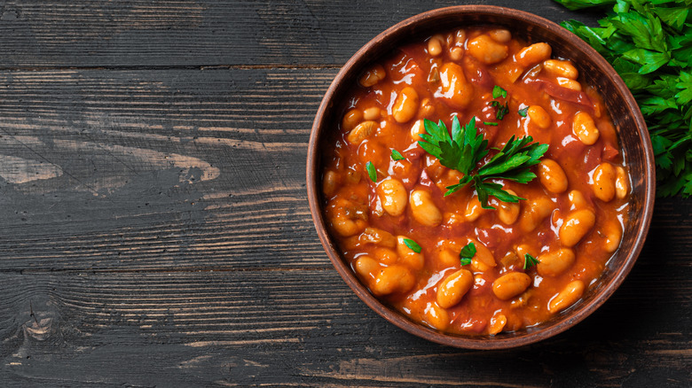 A bowl of beans in a thick red sauce in a brown bowl on a rustic wooden table