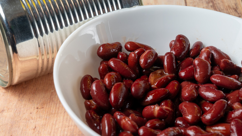 A white bowl of red kidney beans next to a can