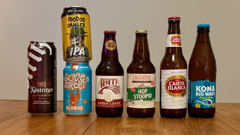 Seven beers lined up on a wooden table., including Lagunitas Stoopid, Voodoo Ranger IPA, and Love Street Blonde