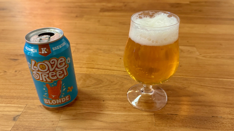A blue can of Love Street with an image of orange hand making a hook 'em sign on the front next to a full glass of the beer.