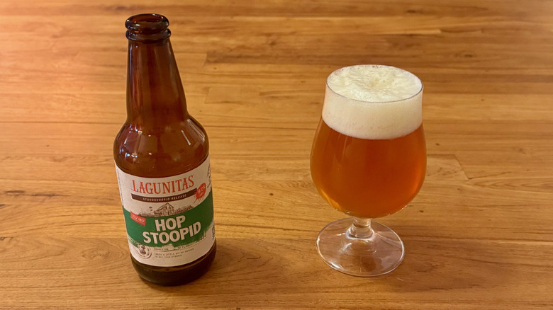 A bottle of Lagunitas Hop Stoopid next to a beer glass filled with amber beer with a foamy head.