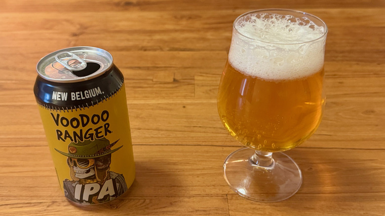 A yellow and black can of Voodoo Ranger IPA next to a full glass of the beer.