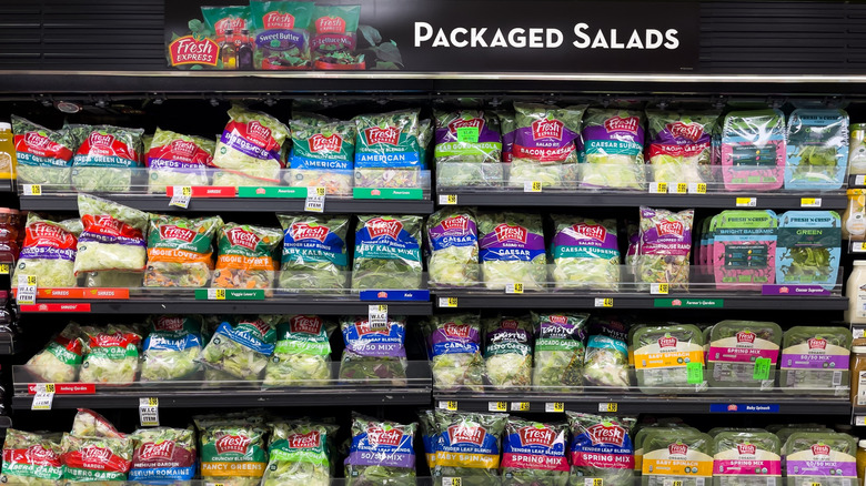 An open refrigerator case with bagged salad on display.