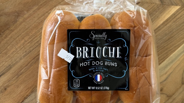 Package of Specially Selected Brioche Hot Dog Buns, an Aldi private label bakery product, displayed on a wooden tabletop with branded packaging visible
