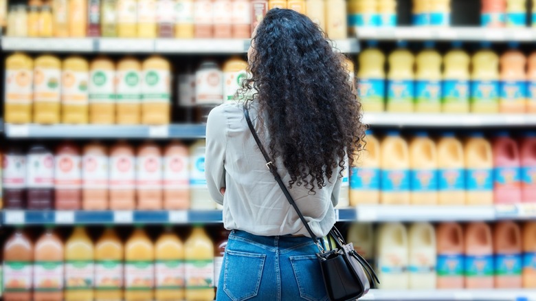 back view of woman customer looking at blurred shelves of various brands in background of grocery store