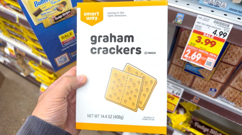 Hand holding a package of Smart Way graham crackers in grocery store aisle