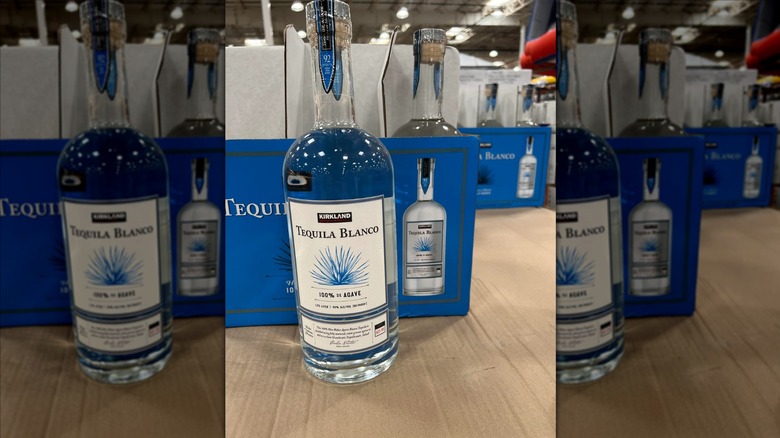 Bottle of Kirkland Signature Tequila Blanco in front of several boxes of the tequila at a Costco warehouse