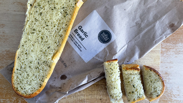 Whole Foods half garlic bread loaf on its bag beside a few individual slices