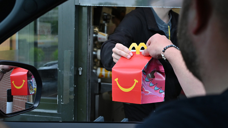 Worker handing McDonalds happy meal out of window to man in car