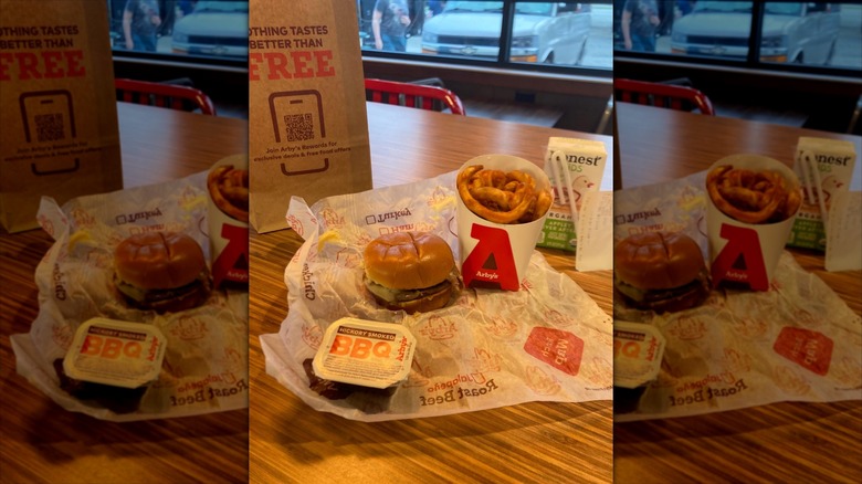 Arbys kids meal spread out on table inside Arby's restaurant featuring a burger, onion rings, and a box of Honest kids' apple juice