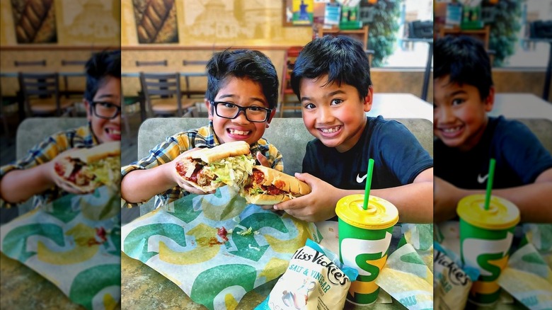 Two kids smiling and holding subs in subway restaurant