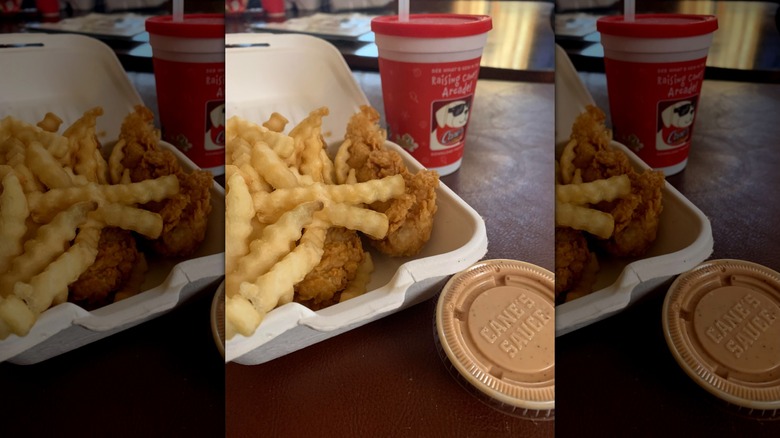 Raising Canes kids meal on table with cane's sauce in plastic ramekin featuring chicken tenders, fries, and a drink