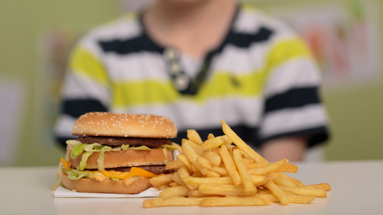 Fast food burger and fry meal close up with young boy stting in background