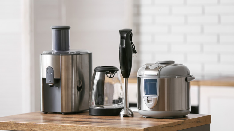 A coffee maker, carafe, immersion blender, and slow cooker on a wooden island in front of a tile backsplash