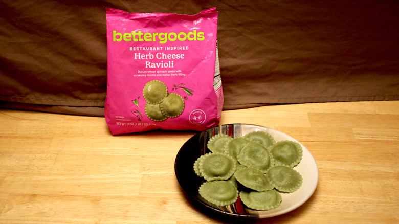 A cooked plate of Bettergoods brand Herb Cheese Ravioli placed beside the bag it came in