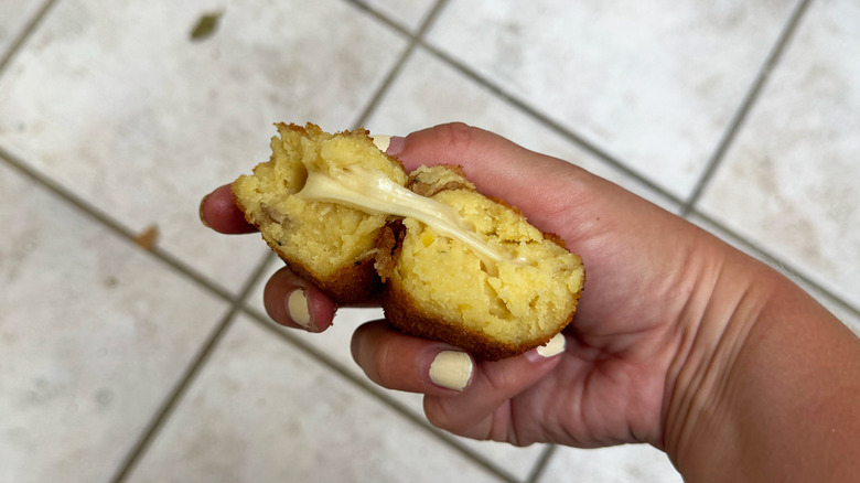 Hand holding crocche di patate mashed potato ball with cheese, tile floor in background