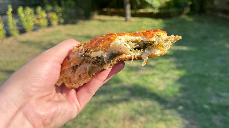 Hand holding escarole pie with park in background