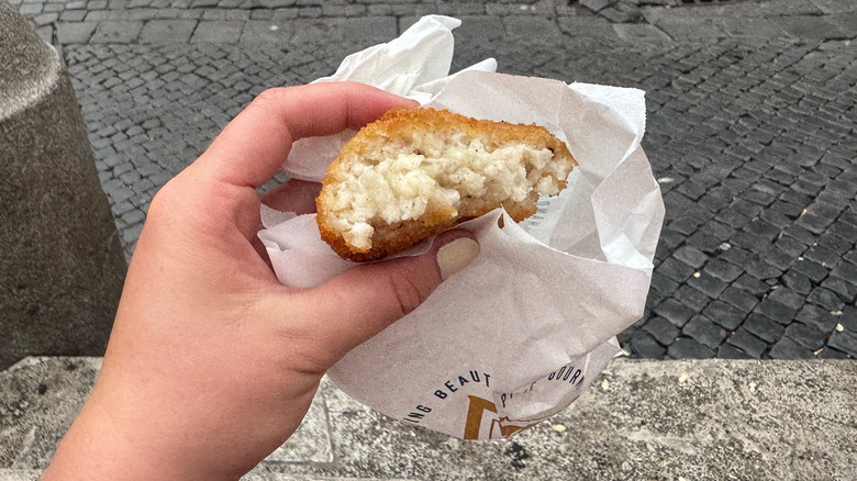 Hand holding cacio e pepe arancini with Naples street in background