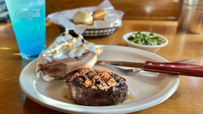 Texas Roadhouse food including steak, sweet potato, rolls, and green beans with blue drink