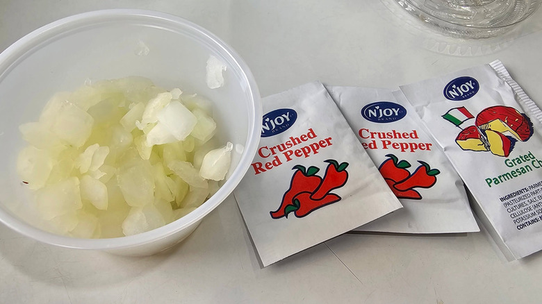 A side bowl of chopped onions next to red pepper and parmesan packets from Costco