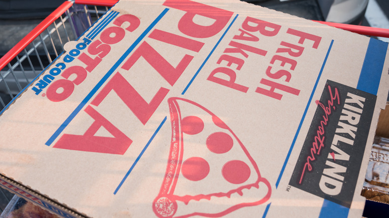 A Costco pizza in a to-go box sitting on top of a cart.