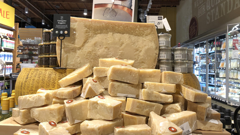 Wedges of Parmesan wrapped in plastic and stacked in front of a half wheel in cheese in a Whole Foods store display