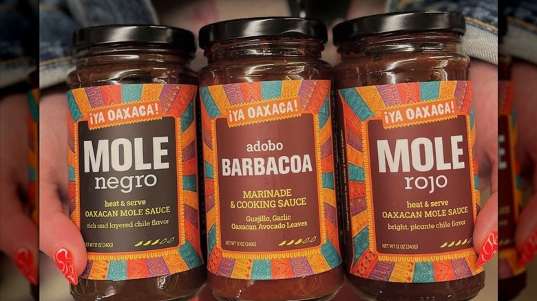Close-up shot of three glass jars with colorful labels containing mole and barbacoa sauces