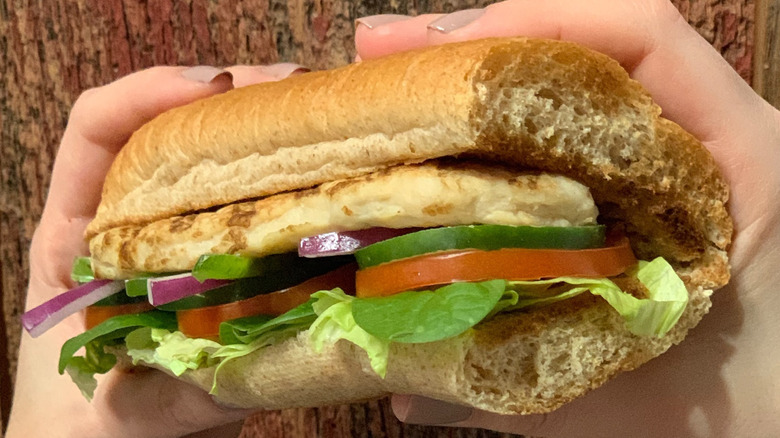 Hand holds up Grilled Chicken Sub with tree in backdrop