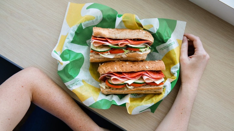 Person sits at counter with sliced Subway sandwich in front of them