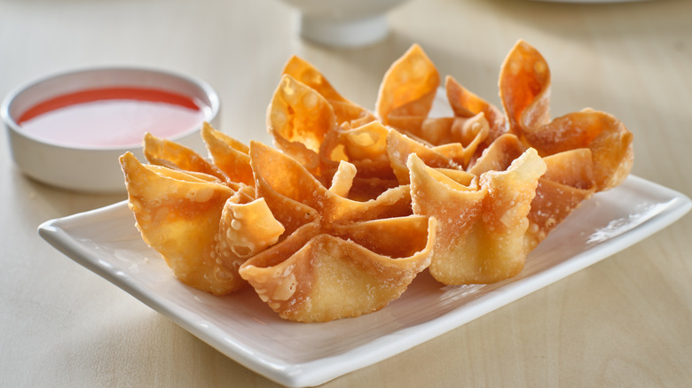 Crab rangoon on white plate with dipping sauce