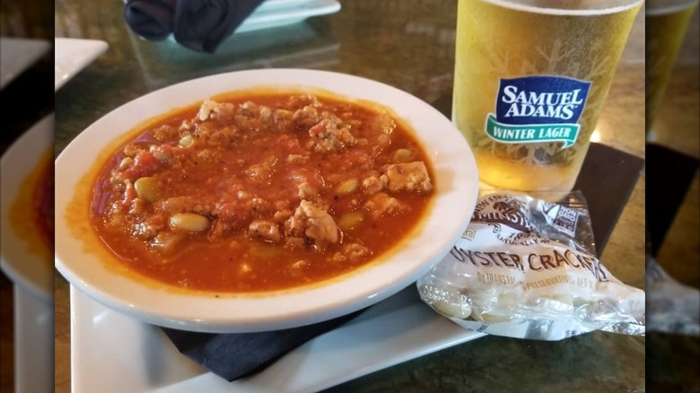 A bowl of mulligan stew next to a glass of beer and some oyster crackers