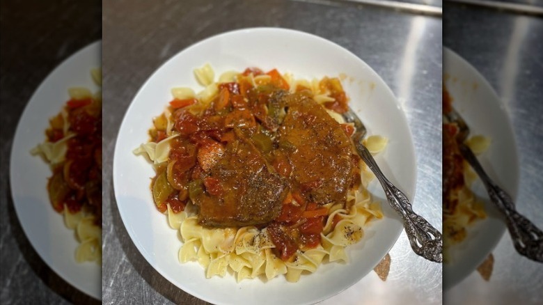 A plate of Swiss steak served over pasta