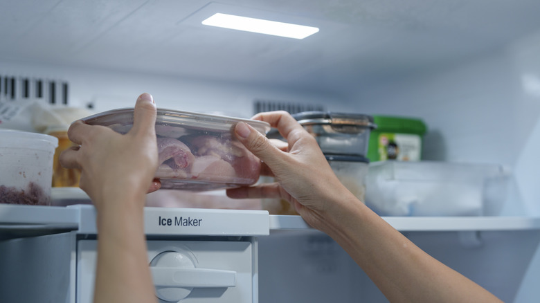 Person putting a container of raw chicken in the freezer