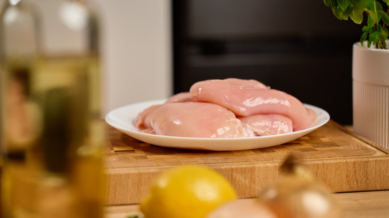 raw chicken on white plate on butcher block