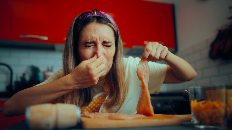 woman both holding nose and also a piece of raw chicken