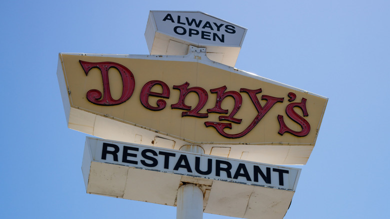 A vintage roadside Denny's sign against a clear blue sky