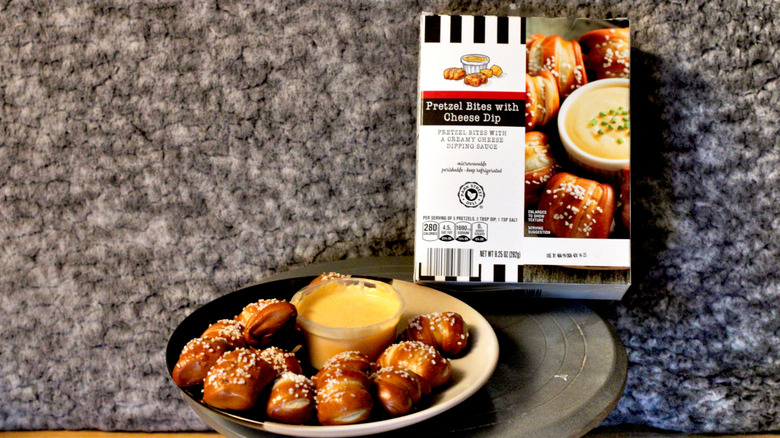 A plate of Park Street Deli Pretzel Bites with Cheese Dip beside the container they came in