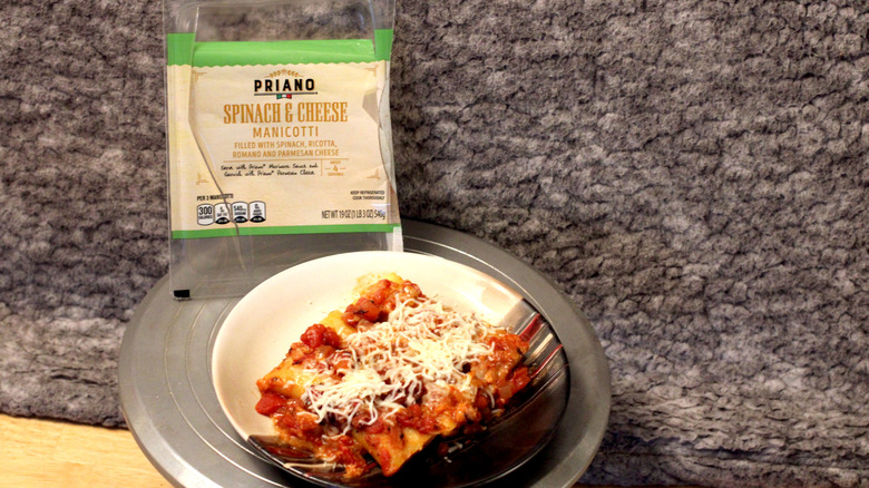 A plate of Priano brand spinach and cheese manicotti with tomato sauce and cheese beside the empty package they came in