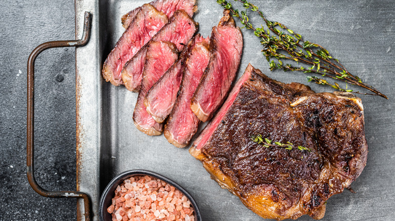 Rare grilled steak on a silver tray by a sprig of rosemary